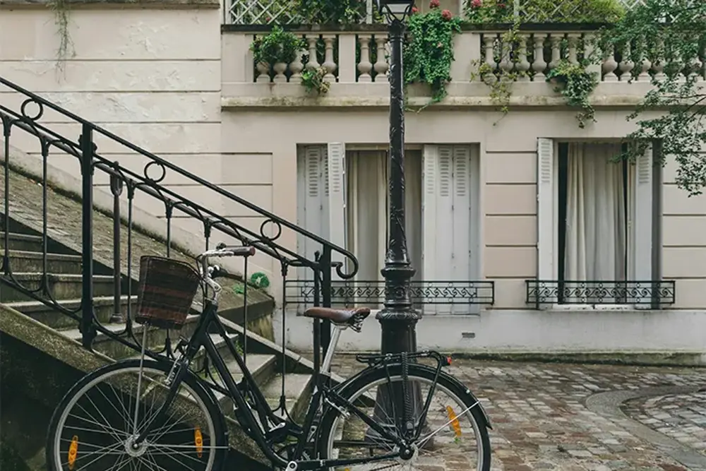 Cykel vid en trappa framför ljus fasad med vita fönsterluckor